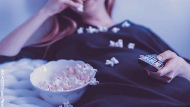 Foto de una mujer acostada sobre la cama comiendo palomitas de maíz que muestra las películas recomendadas en Netflix