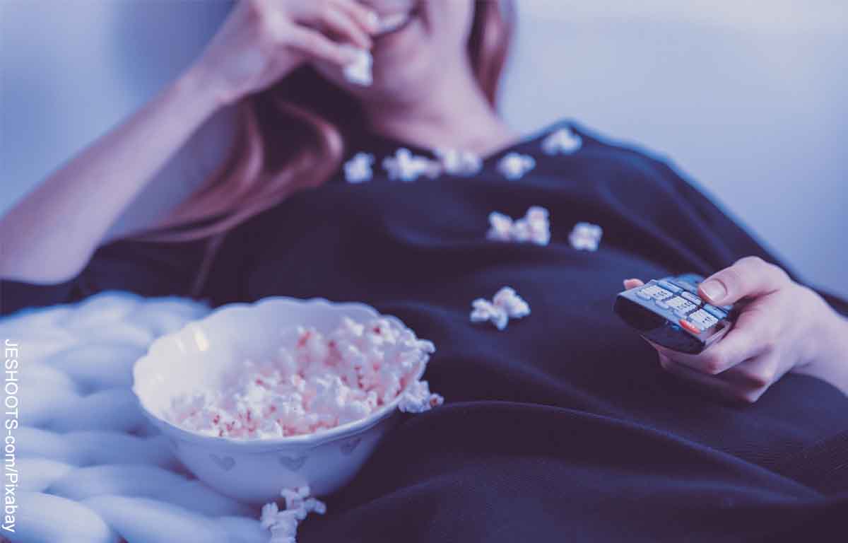 Foto de una mujer acostada sobre la cama comiendo palomitas de maíz que muestra las películas recomendadas en Netflix