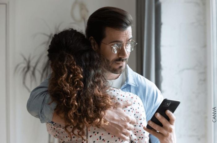Foto de un hombre abrazando a su pareja y revisando el celular