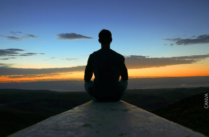 Foto de un hombre sentado frente al amanecer