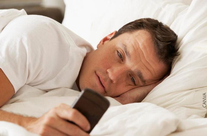 Foto de un hombre en la cama mirando su celular