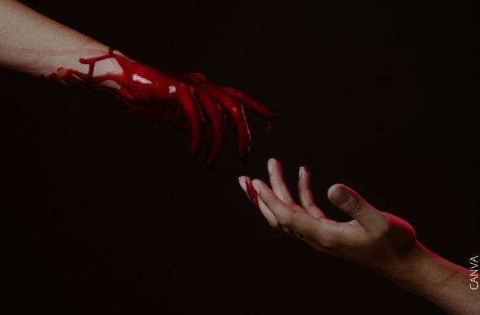 Foto de una mano llena de sangre y otra a punto de tocarla