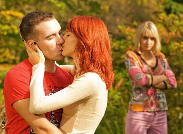 Foto de pareja besándose mientras los observa una mujer.