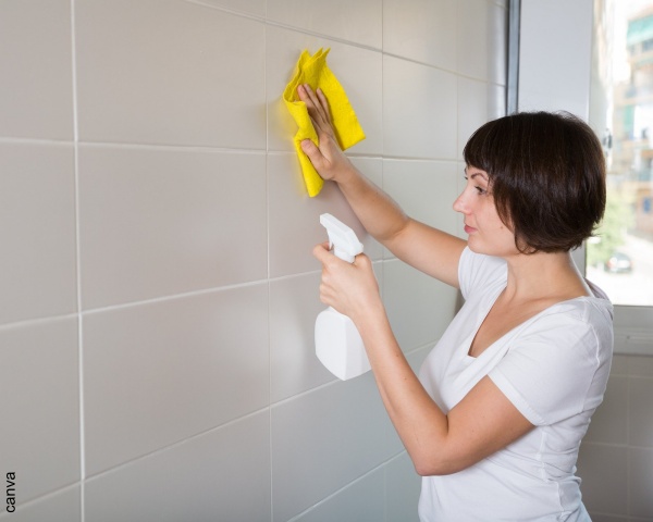 Foto de mujer limpiando pared blanca de baldosa.