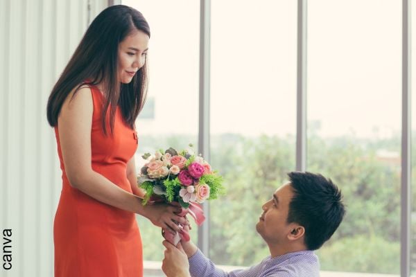 Foto de hombre entregando flores a una mujer arrodillado.