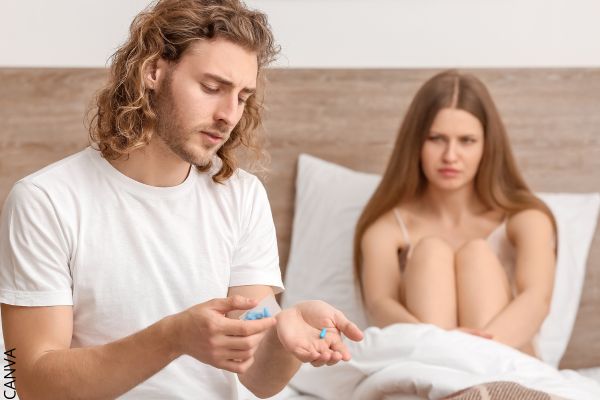 Foto de hombre con pastilla azul en la mano y mujer sentada sobre una cama.
