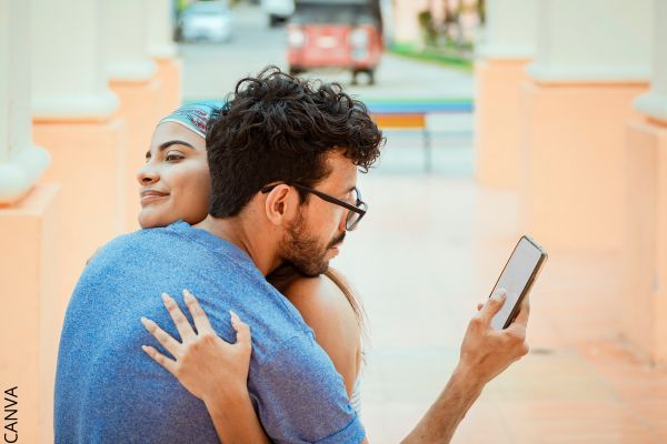 Foto de hombre abrazando a una mujer mientras mira el celular.