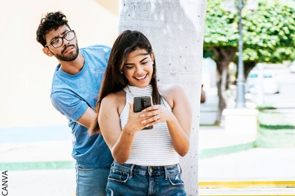 Foto de mujer sonriendo al celular y hombre tratando de espiarla.