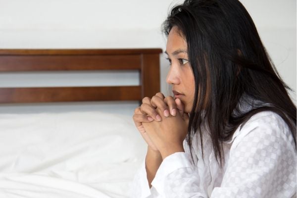Mujer rezando frente a una cama.