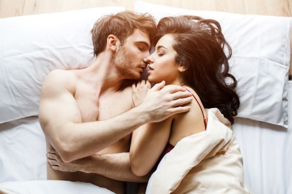 Foto de una pareja acostada en una cama acariciándose apasionadamente