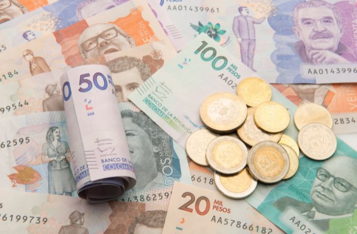 Foto de muchos billetes sobre una mesa con un billete enrollado encima y muchas monedas sobre ellos.