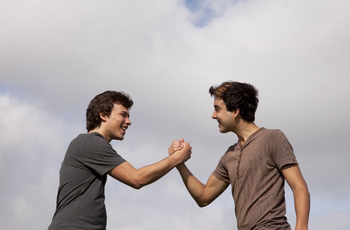 Foto de dos hombres tomados de la mano afianzando la amistad con nubes atras