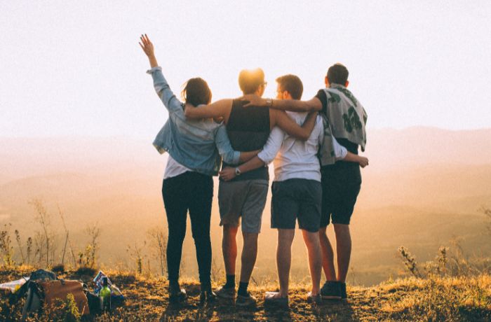 foto de cuatro amigos abrazados en una montaña con un atardecer de fondo