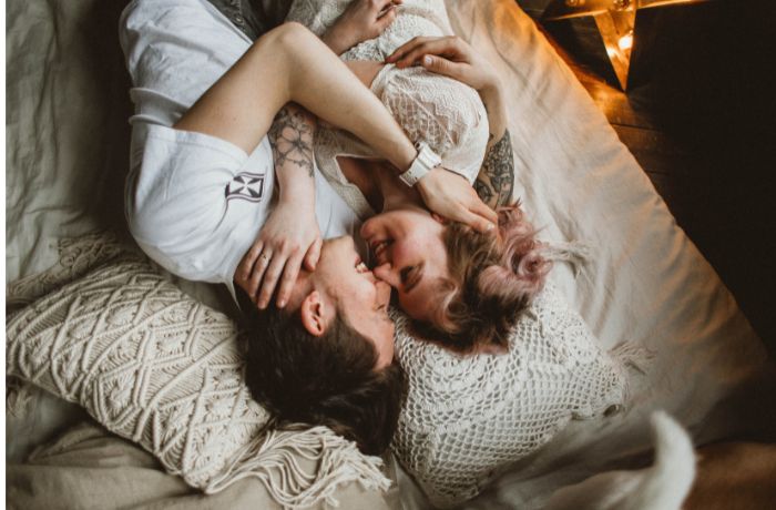 Foto de una pareja acostada en una cama abrazada y con la cara muy cerca