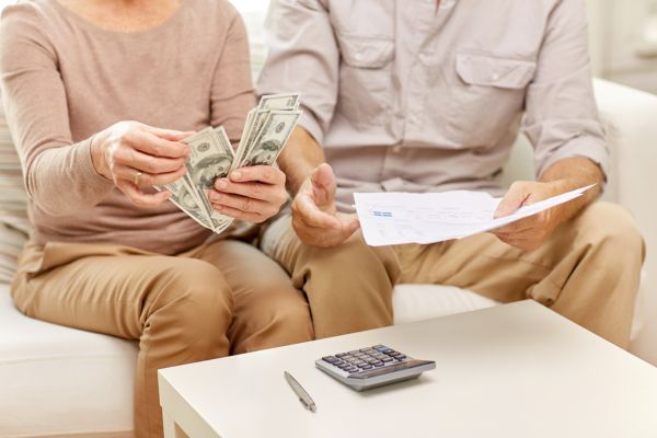Foto de una pareja haciendo cuentas con dinero y facturas en la mano y una calculadora junto a un bolígrafo en la mesa