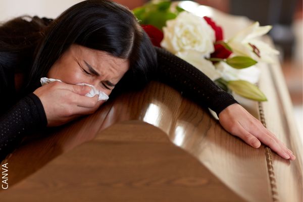 Foto de mujer llorando sobre un ataúd.