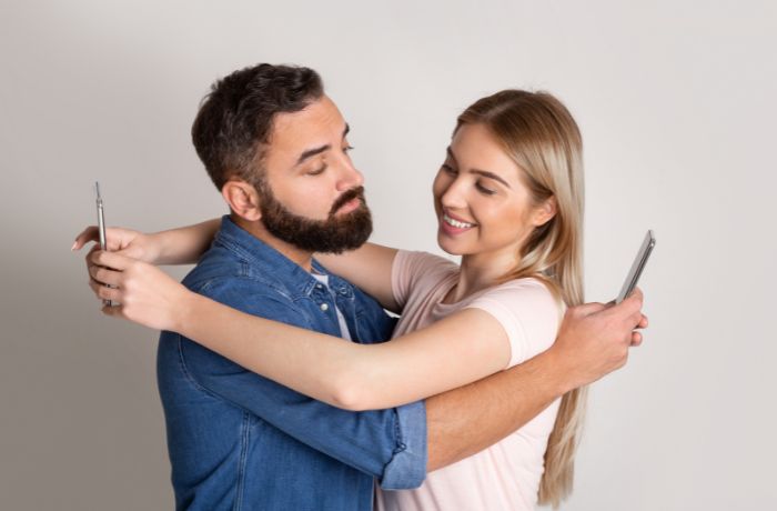 Foto de una pareja abrazada y cada uno esta en el celular