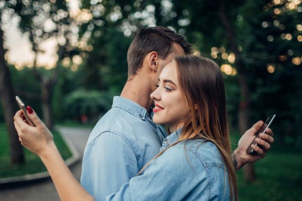 Pareja abrazada y mirando el celular cada uno