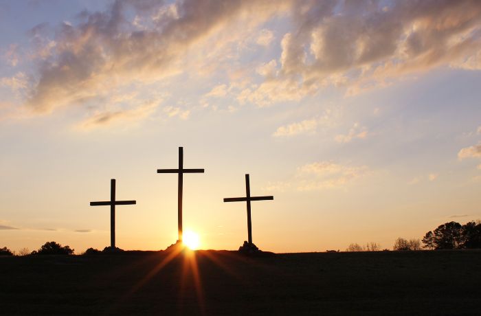 Foto de tres cruces en medio de un valle con la puesta de sol atras.