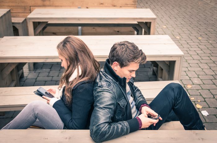 Foto de una mujer y un hombre en un patio donde no se comunican y están mirando el celular