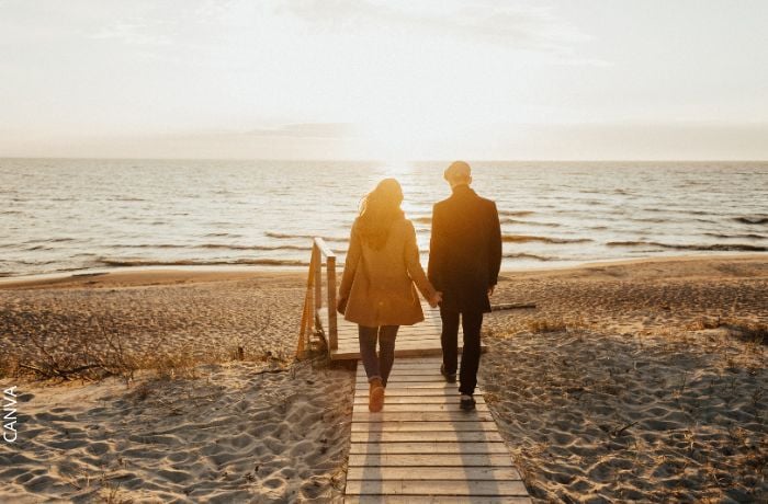 Foto de un hombre caminando de la mano de una mujer frente al mar.