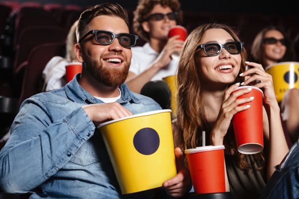 Foto de personas en una sala de cine con gafas 3D, comiendo palomitas de maíz y tomando una bebida de un vaso rojo